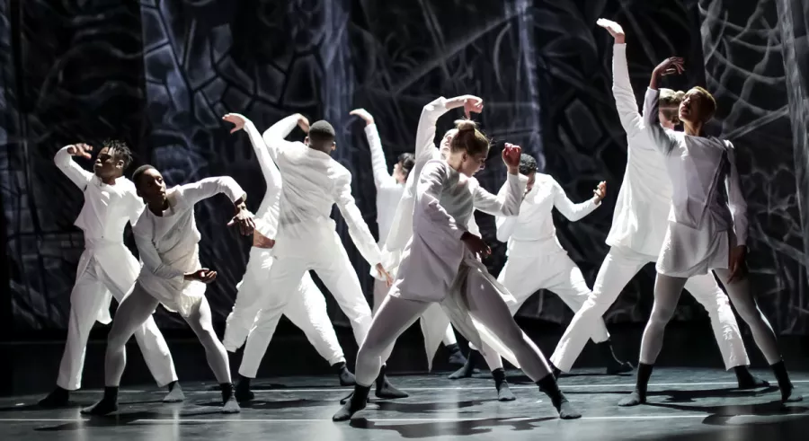 Dancers in white outfits performing on stage with an abstract dark background.