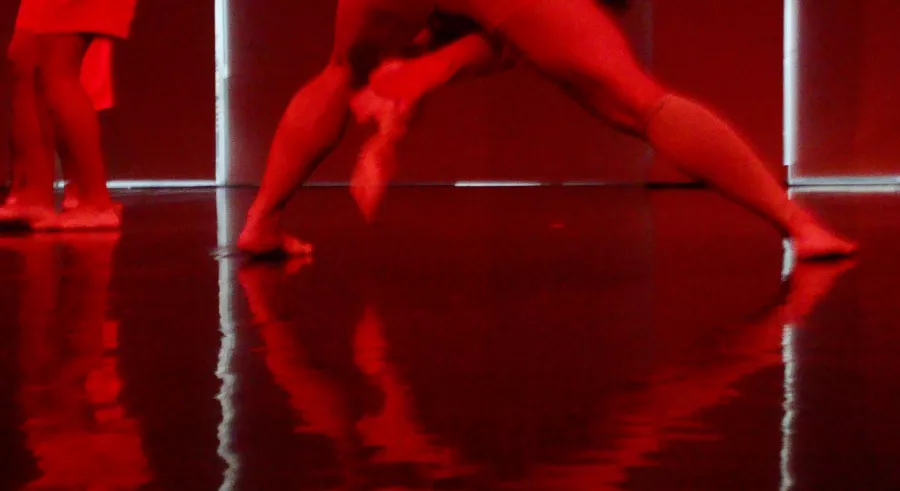 The floor's reflection of two dancers dancing with only their legs and feet visible in red lighting.