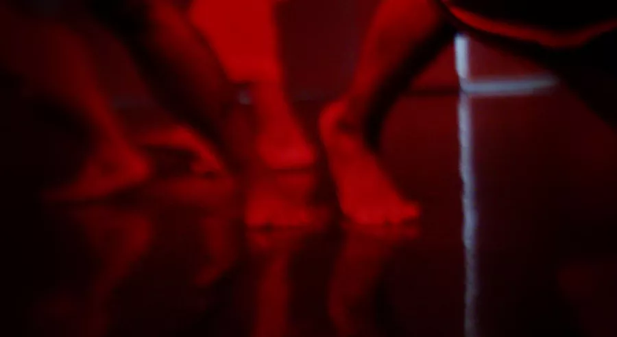 Dancers' feet on a reflective floor with red lighting. 