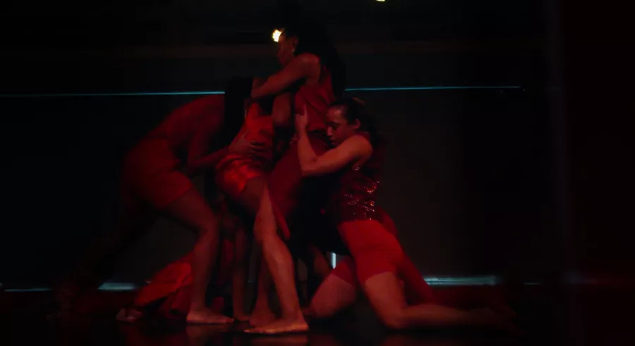 Multiple dancers embrace each other in red lighting.