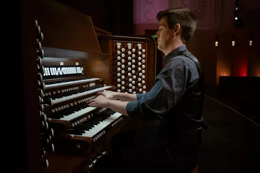 Greg Zelek, a man with short brown hair in a navy button-up, plays the pipe organ.