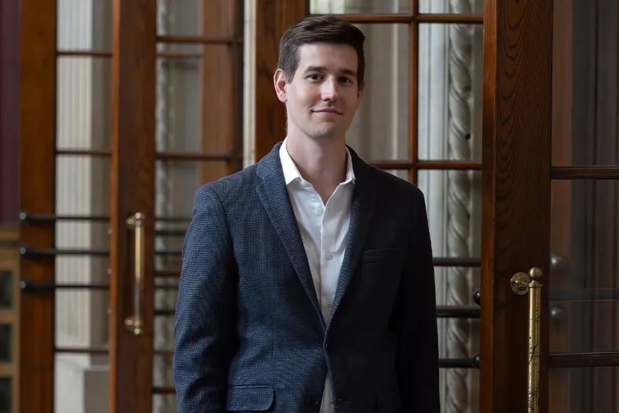 Greg Zelek, a man with short brown hair wearing a navy suit and white button up, smiles softly.