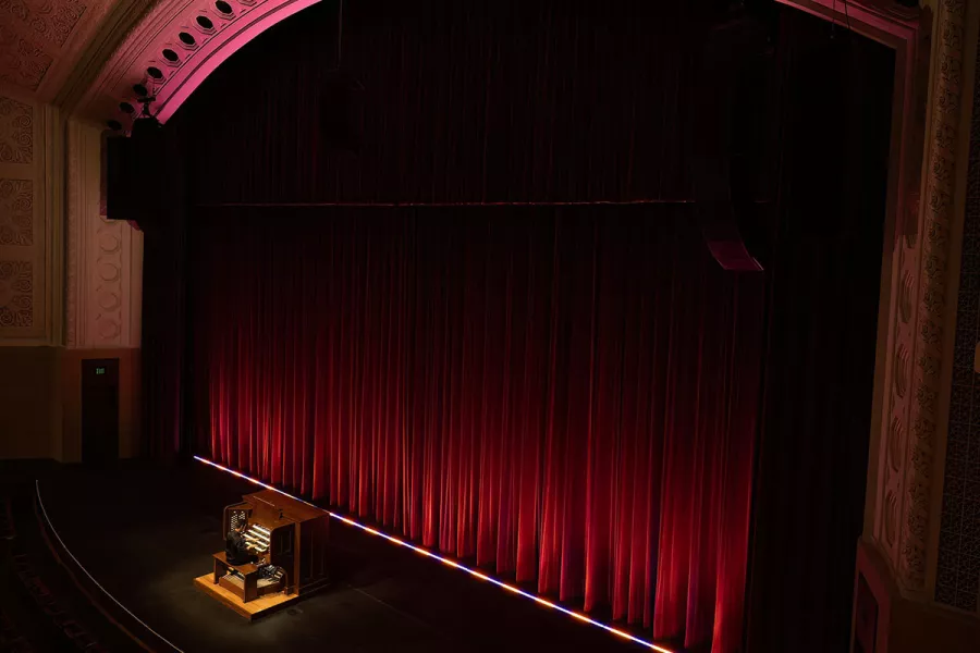 Balcony view of Greg Zelek playing the pipe organ on the Northrop stage in front of a red curtain.