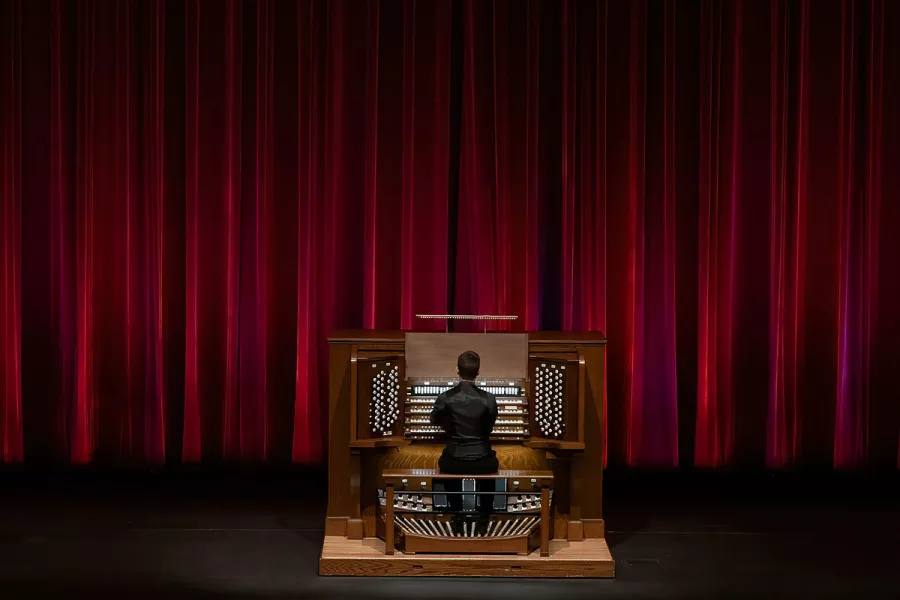 Greg Zelek playing the pipe organ on the Northrop stage in front of a red curtain.