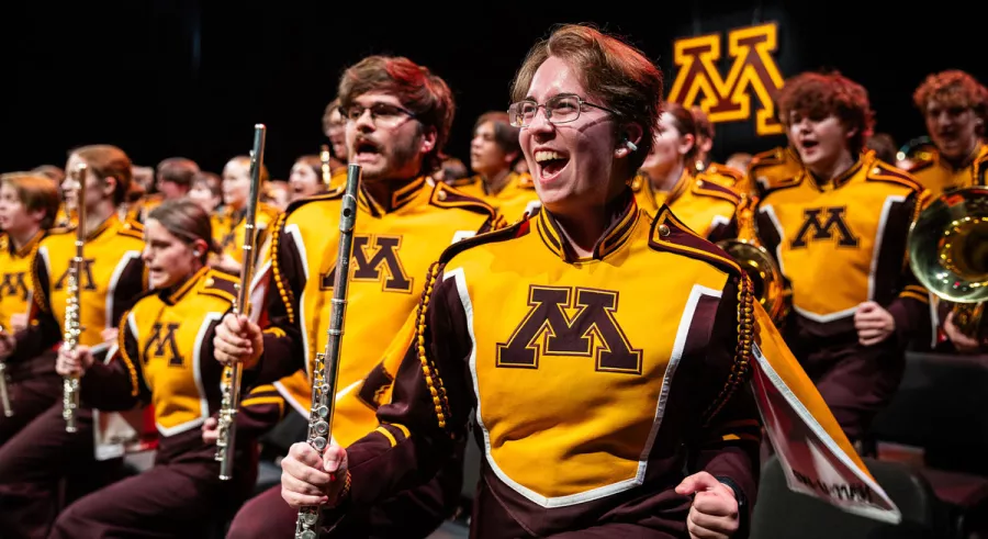 UMN Marching Band flute players smiling and laughing in their seats onstage. 