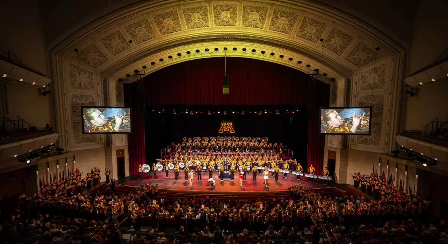 The view from the back of the auditorium of the entire UMN Marching Band onstage in front of a full audience. 