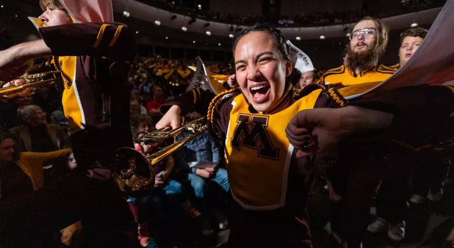 A close-up on a member of the UMN Marching Band smiling and cheering. 