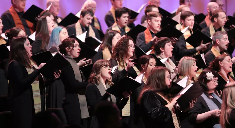 Choir members singing with folders in their hands.