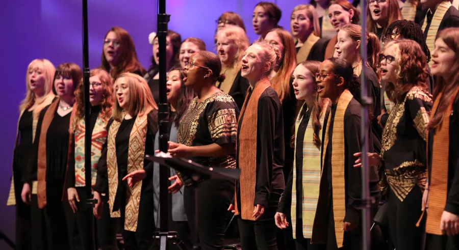 Young choir members singing in front of a purple background.