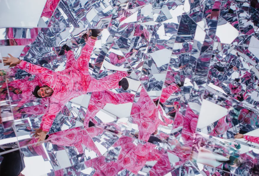 Nur-D in a pink suit surrounded by mirror fragments