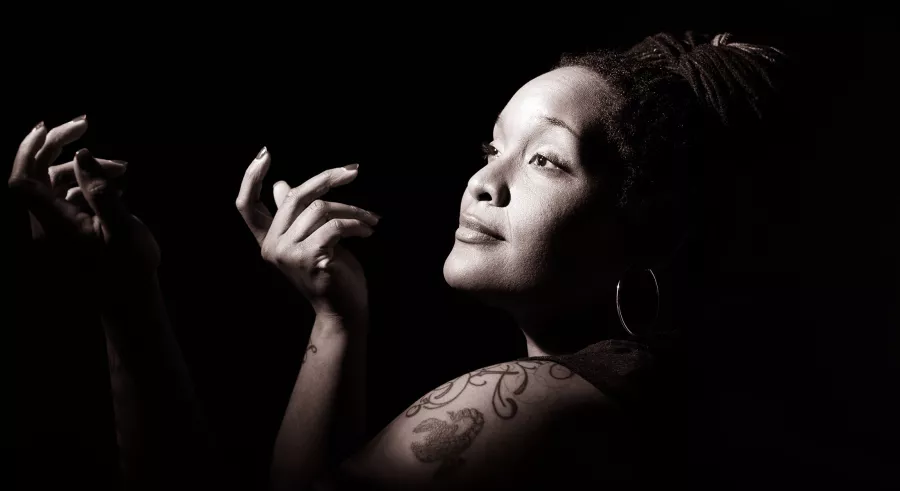 Black and white image of PaviElle in profile, light on her face, shoulder and hands.