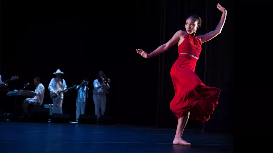 A dancer in a red skirt on stage with four dancers in white in the background