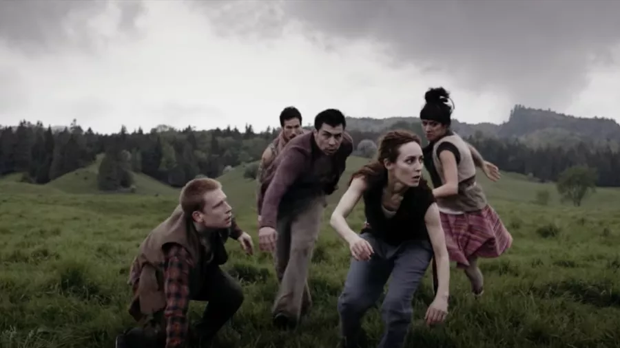 Modern dancers running outside on green grass with a gray sky