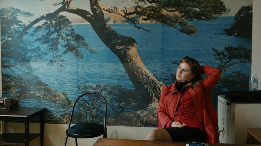 A woman in a red jacket against a wallpapered wall with water and a tree