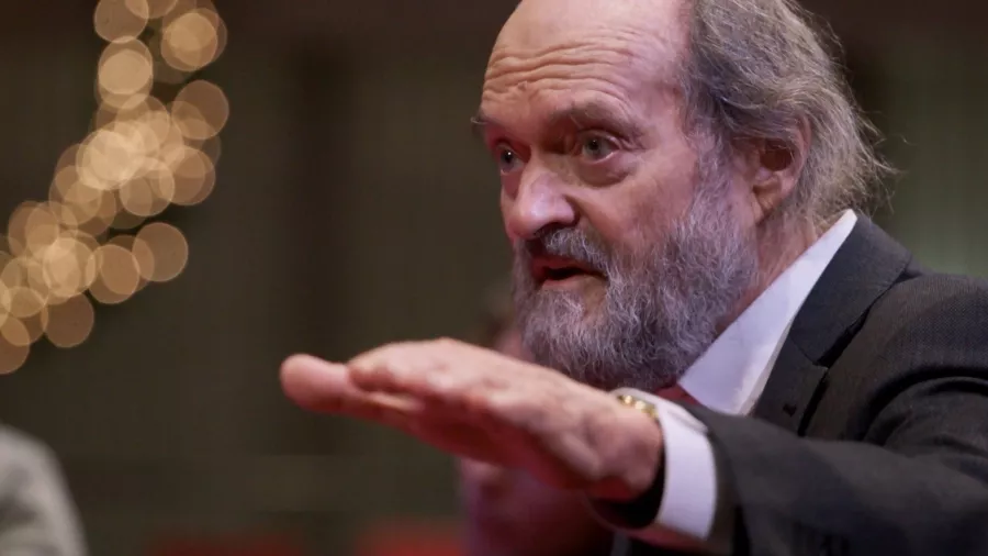 An older man with a gray beard holding out his hand