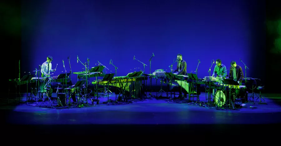 A blue lit stage shows a horizontal line of instruments including drum sets and keyboards.