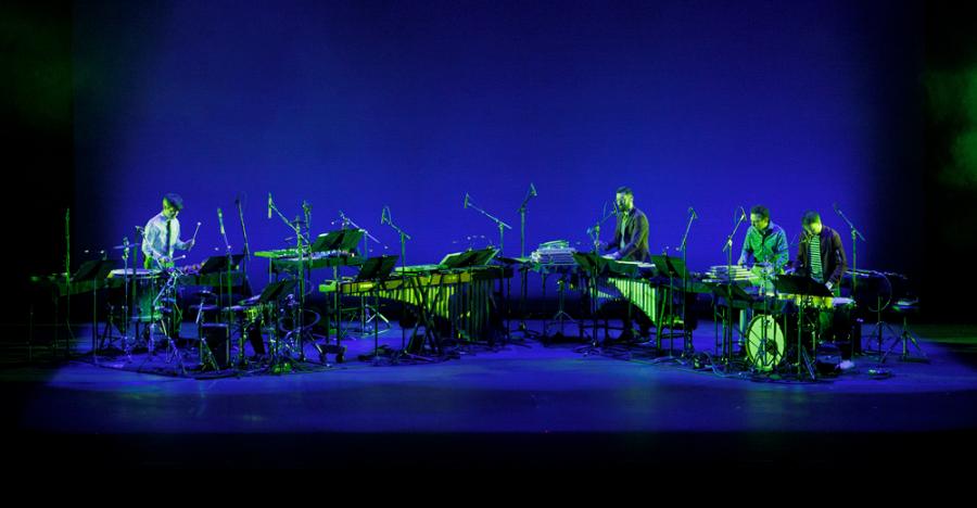 A blue lit stage shows a horizontal line of instruments including drum sets and keyboards.