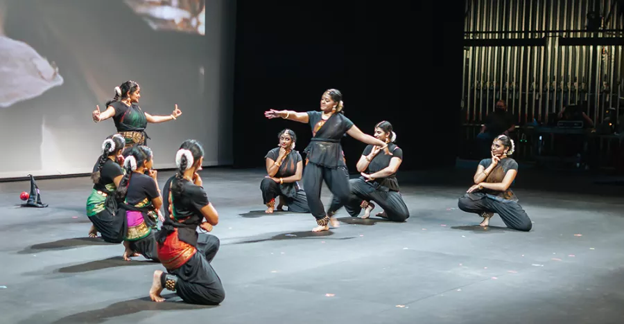 Dancers on stage are wearing all black traditional costumes.
