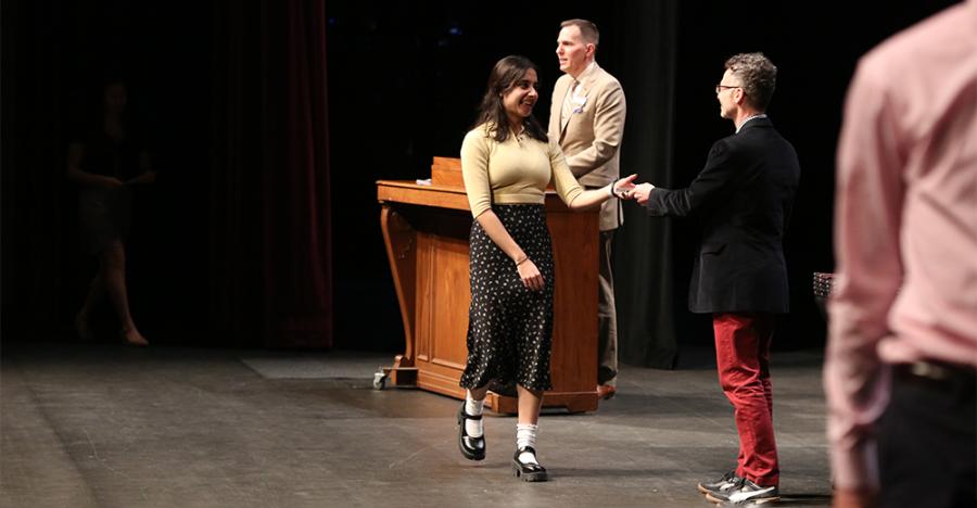 Photograph of a student walking across the Northrop stage. They are giving another person a handshake. 