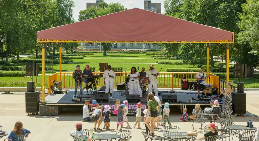 Musical group Funktion Junction plays on the Northrop Plaza stage for audience members outside. A group of children stand right in front of the stage. 