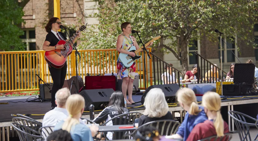 Musical duo Suzy Plays Guitar play for an audience on the Northrop Plaza Stage, both playing guitar and singing into microphones.