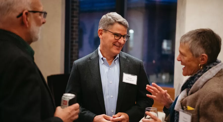 Three people in conversation. Person wearing suit smiles.