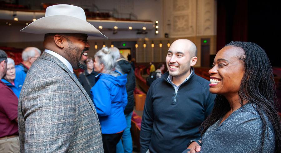 Marshall Johnson in a cowboy hat talking to two smiling people in a blue shirt and a gray shirt in the Carlson Family Stage auditorium.