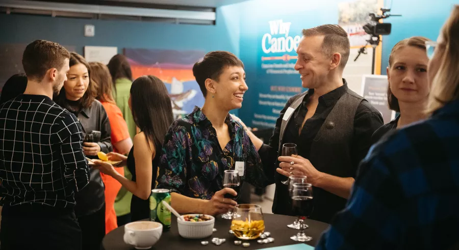 Several people talk and smile around a table while holding beverages.