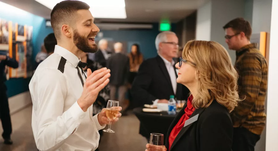 Two people dressed in formal attire talk to one another while holding beverages at a cast party.