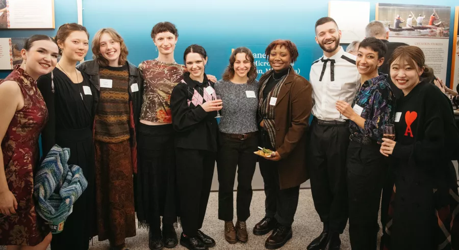 Several people group together and smile for a photo in front of a blue wall in a gallery.