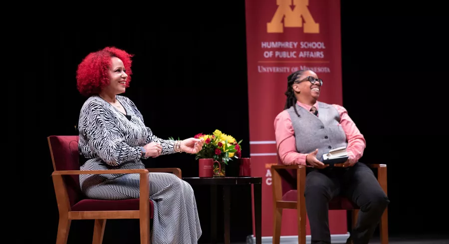 Two people sit onstage beside one another, smiling.