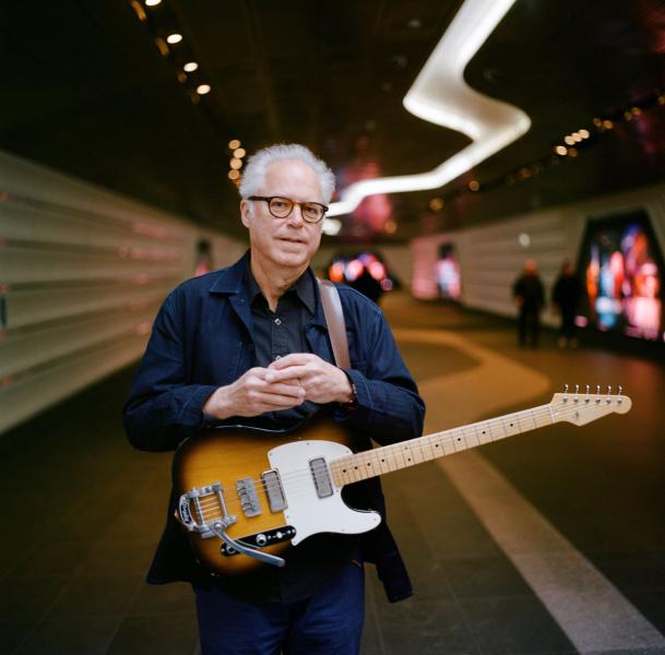 Bill Frisell has his guitar around his shoulder in a hallway