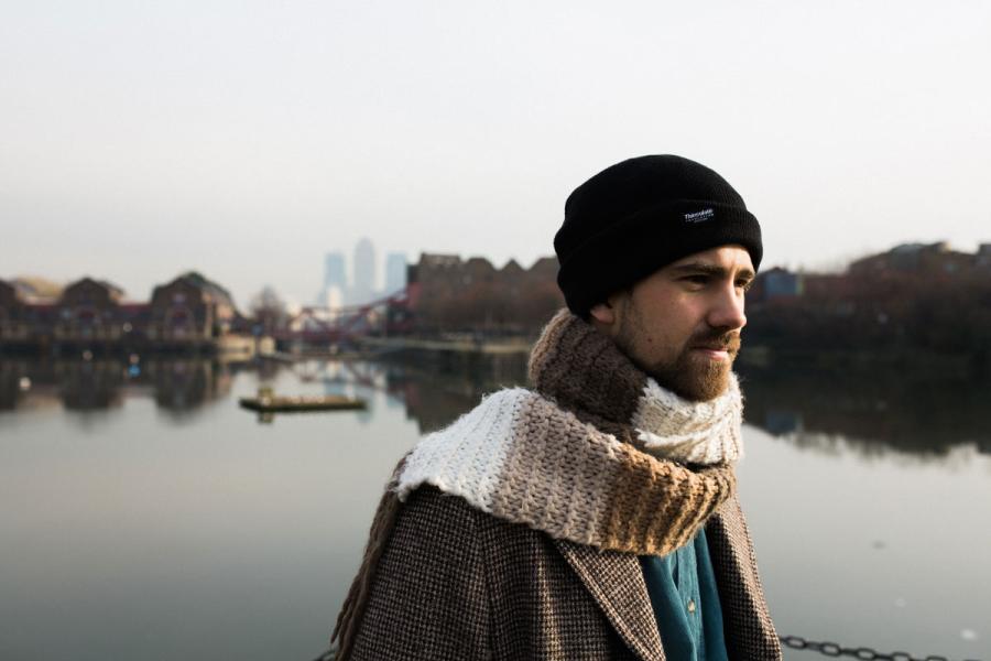 Kit outside by a lake wearing a knit cap and scarf