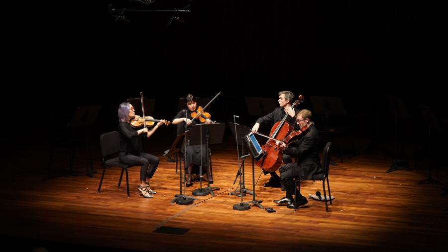 Four members of the Saint Paul Chamber Orchestra sit in a half-circle playing their string instruments on a stage