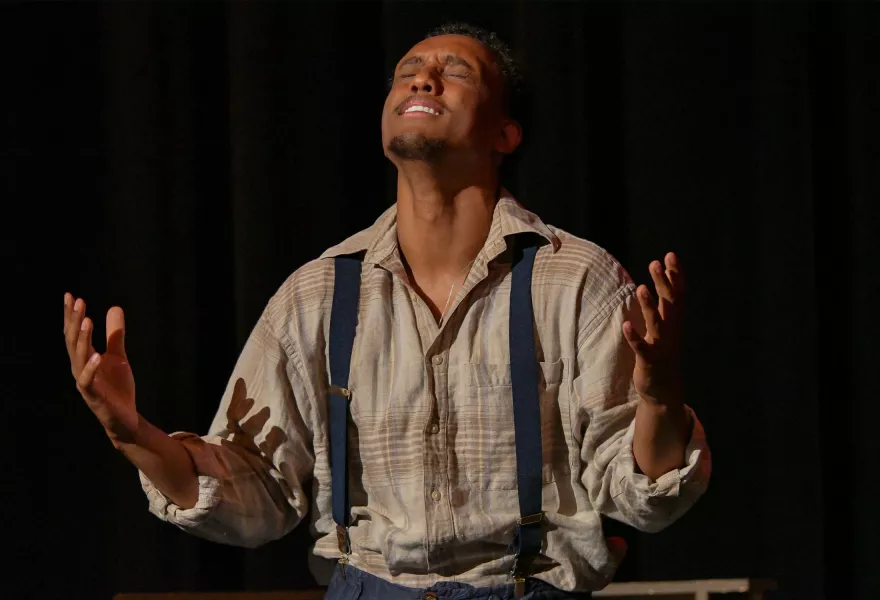 man in plaid shirt and suspenders lifting his face to the sky, eyes closed,  hands open upwards.