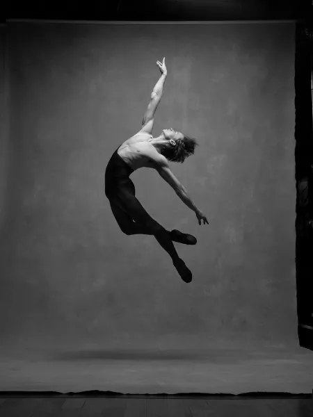 Daniil in black pants jumps with arched back, right arm up, left arm out behind 