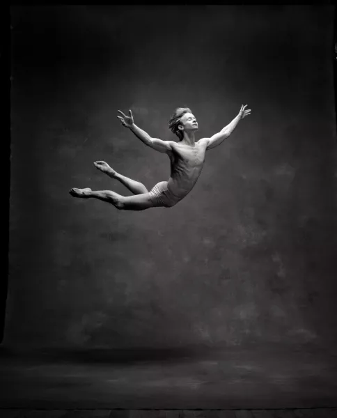 A person jumps into the air with their arms spread wide and a serene look on their face.