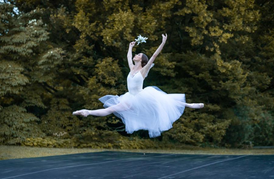 A dancer in a white dress leaps with legs straight out front and back. 