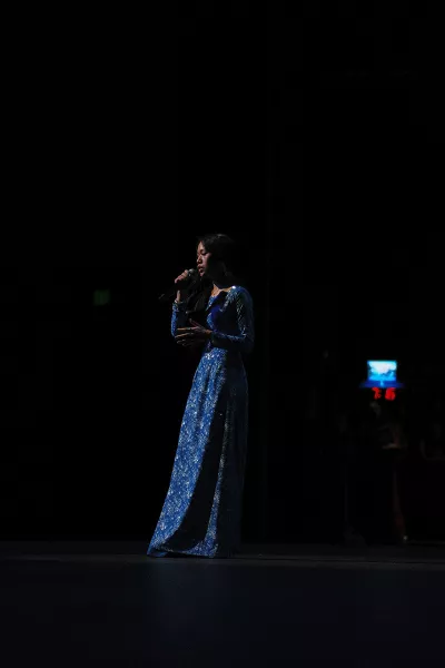 A woman in a blue dress holds a microphone on stage.