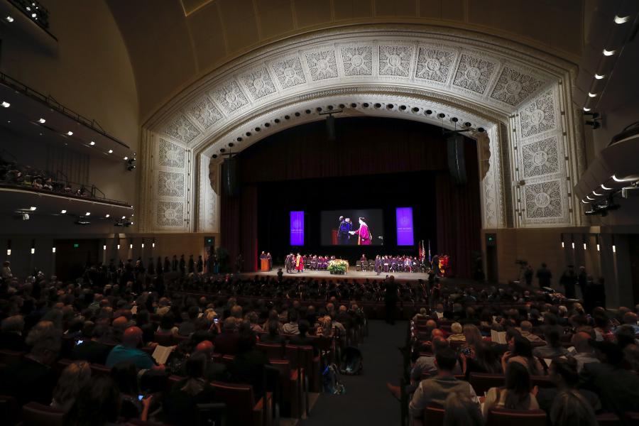 A front-on view of the Carlson Family stage during a graduation ceremony. A beautifully engraved arch is lit up around the stage.