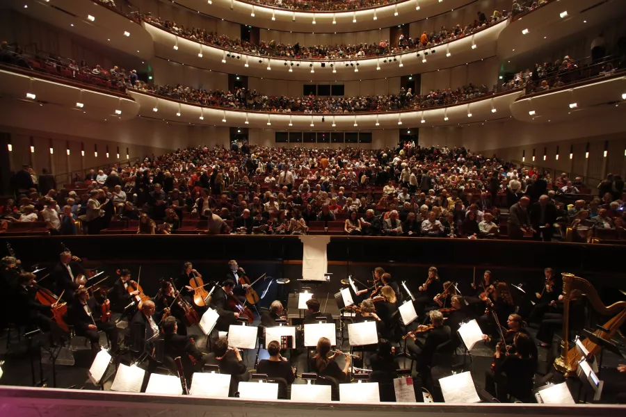 The orchestra pit filled with musicians playing instruments in front of a full audience in the auditorium.