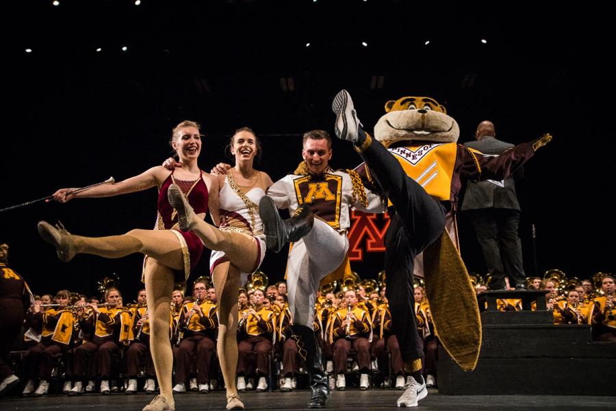 Drum Major team do high-kicks in front of band with Goldy