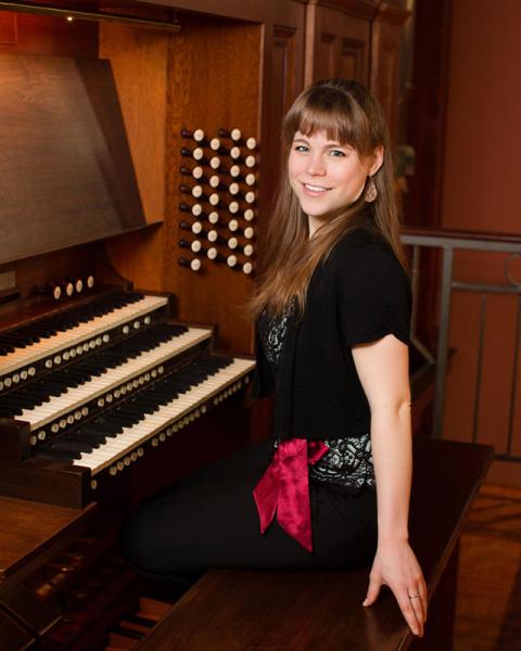 Katelyn Emerson sits at an Organ and smiles towards the camera.