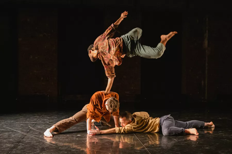 Three male Gallim dancers perform on stage with a black background.