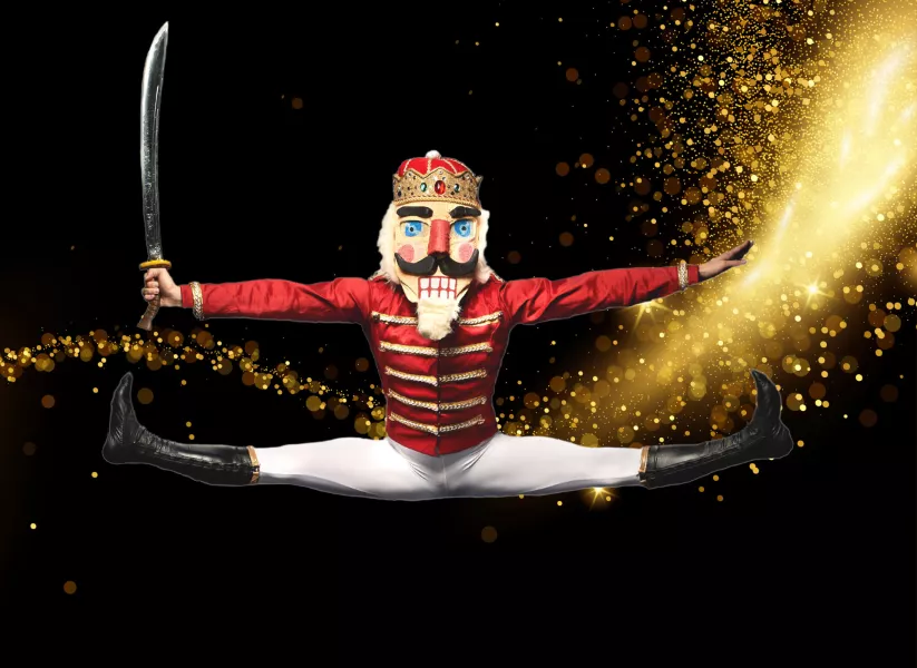 Dance in full center split leap wearing the Nutcracker costume and holding a sword. Sparkles swoosh in the background.