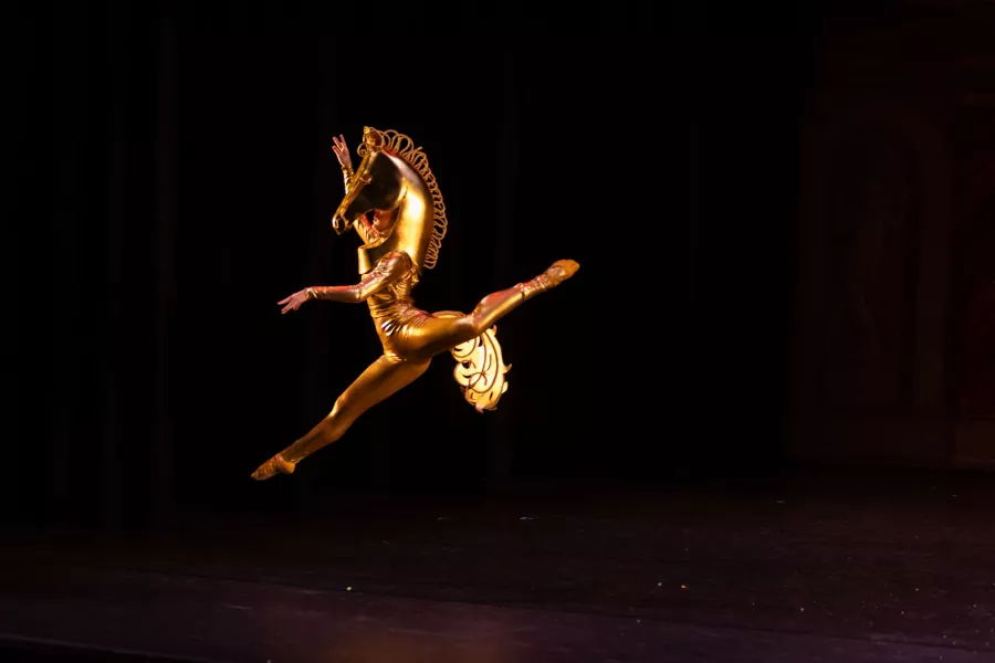 Dancer leaps wearing a gold horse costume
