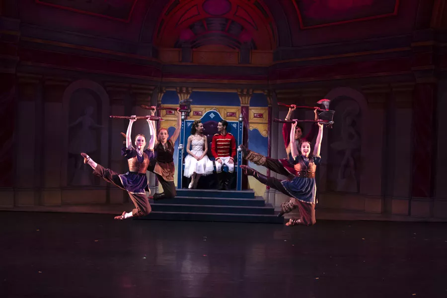 Four dancers leaping in unison holding prop axes.