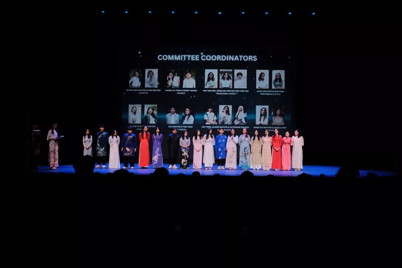 People in a line on the stage wearing different colored outfits.