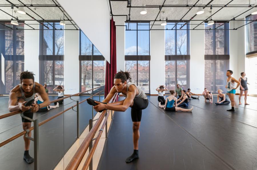 A male dancer stretching at the barre while others warm up behind him
