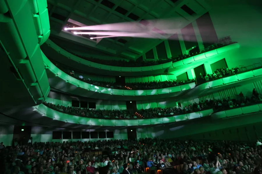 A view of the audience during a rock concert. An emerald green light glows against the balconies full of people.